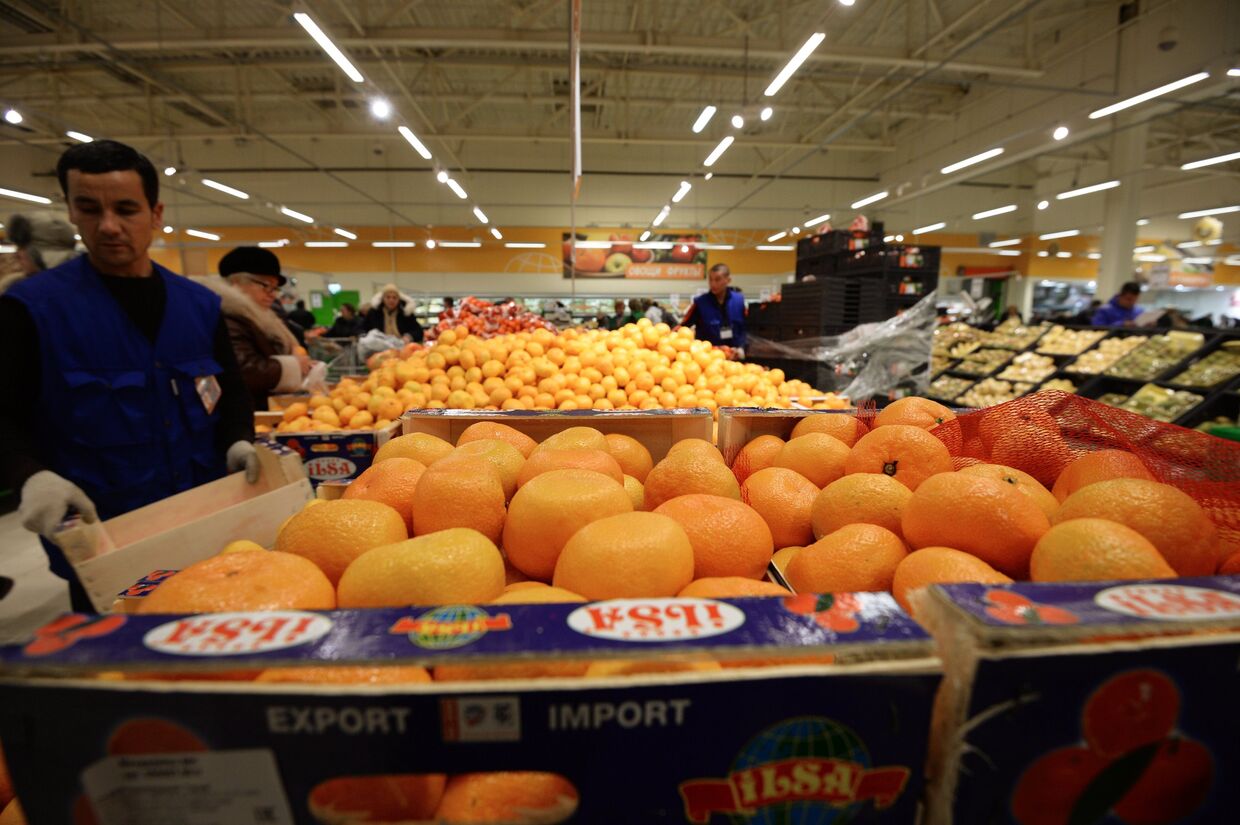Продавец у прилавка с мандаринами из Турции в торговом зале гипермаркета Глобус