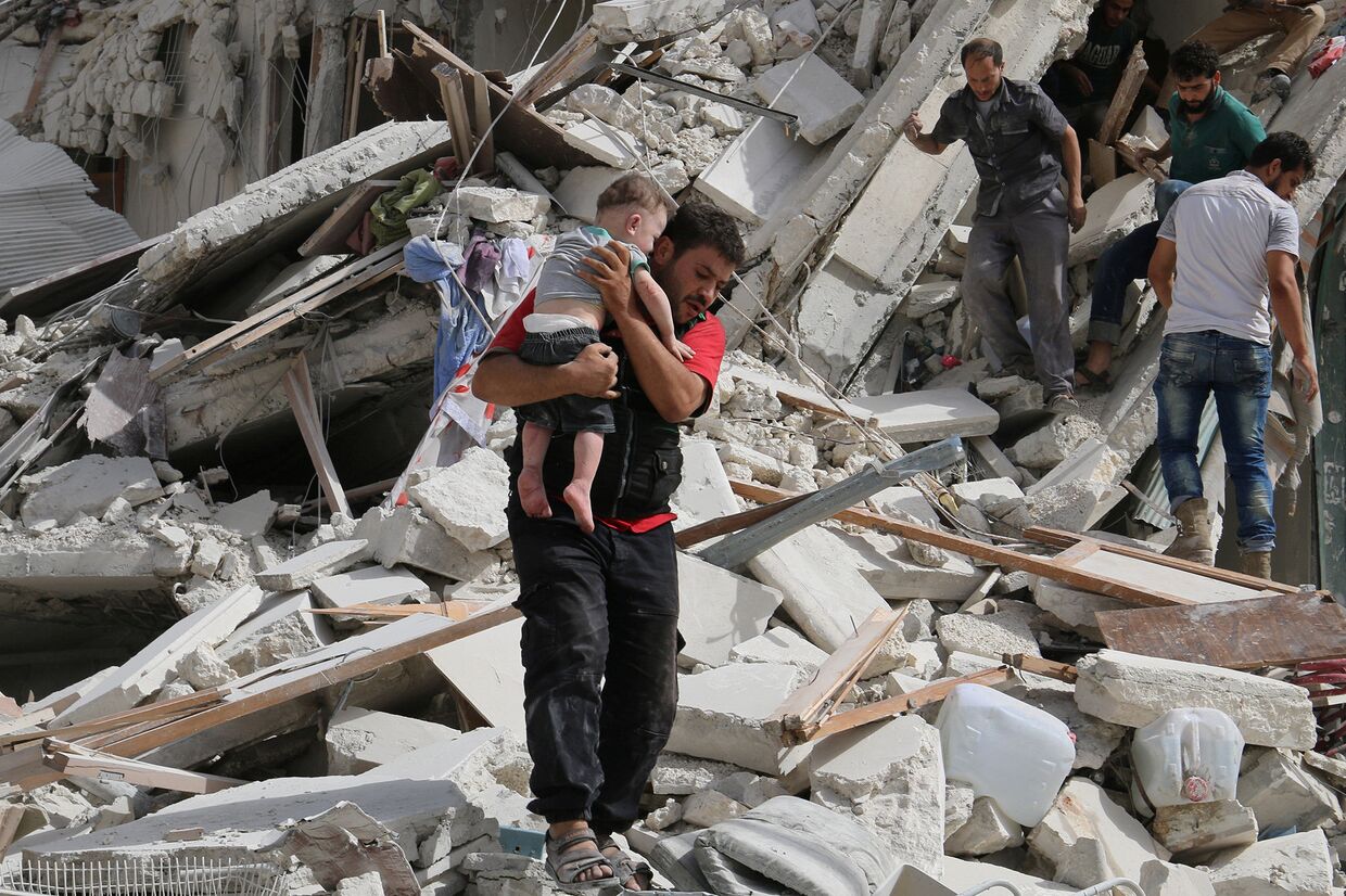 Мужчина несет раненого ребенка после авиаударов в Алеппо