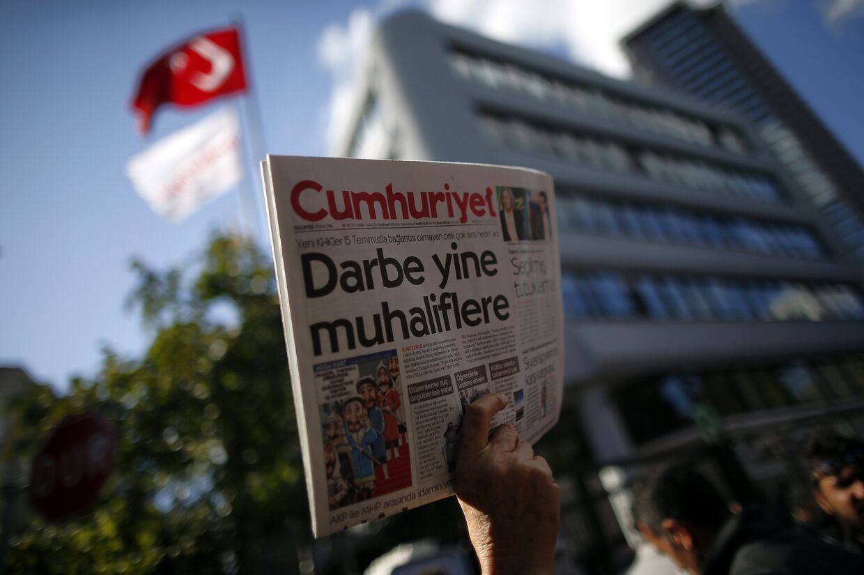 Протестующий с выпуском Cumhuriyet рядом с офисом редакции газеты в Стамбуле, заголовок на первой полосе: «Новый рейд против оппозиции»