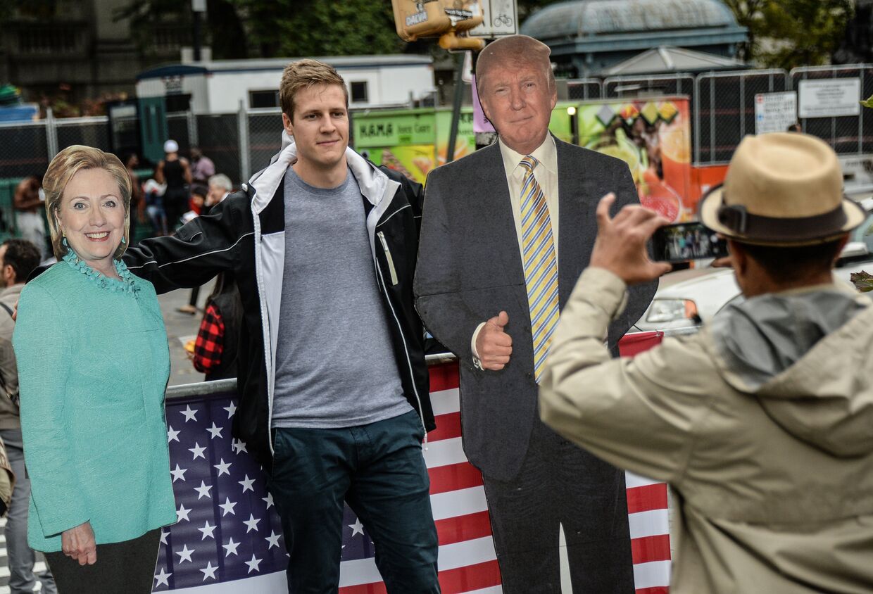 Мужчина фотографируется с ростовыми фигурами кандидатов в президенты США