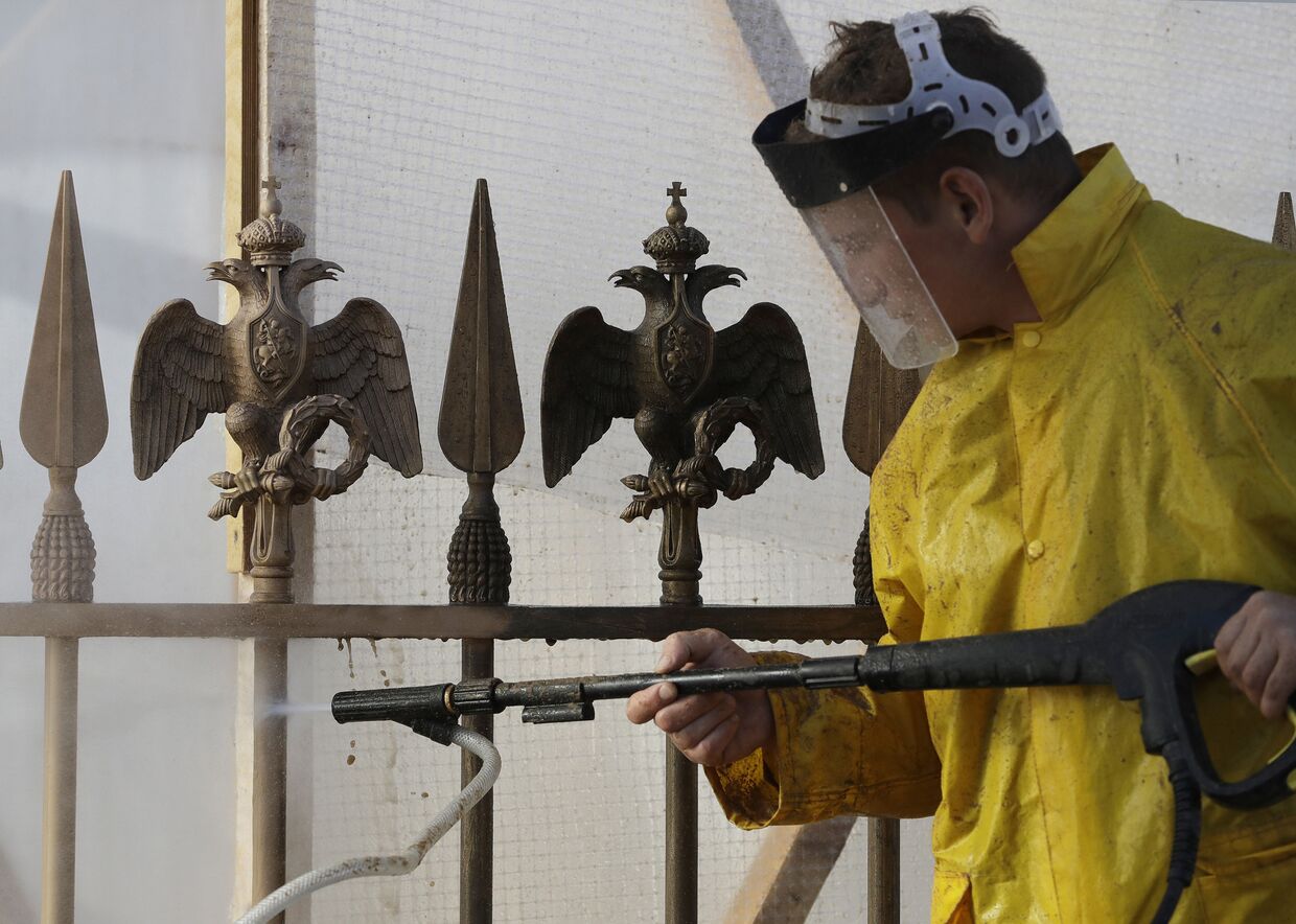 Работник чистит забор с бронзовыми скульптурами двуглавых орлов государственного герба России