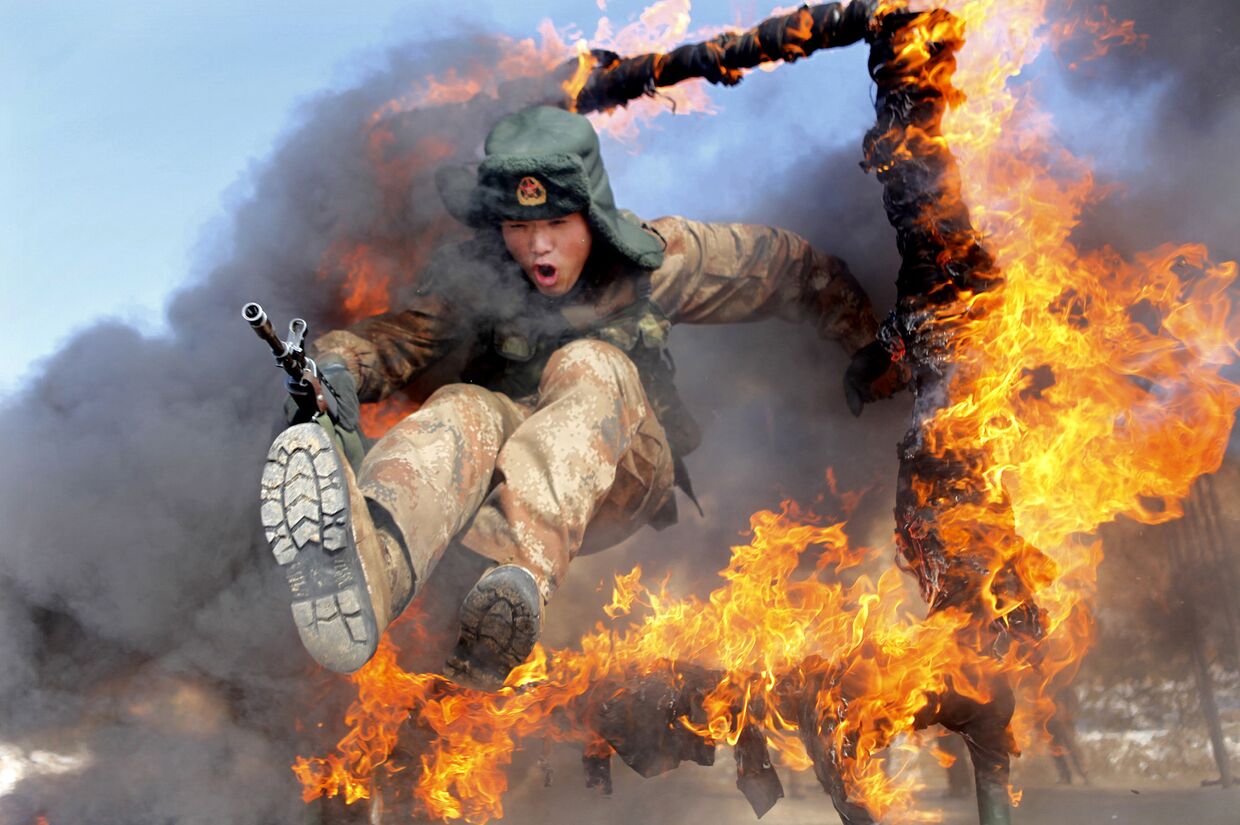 Солдат выполняет прыжок через горящее кольцо во время тактических учений в провинции Хэйхэ