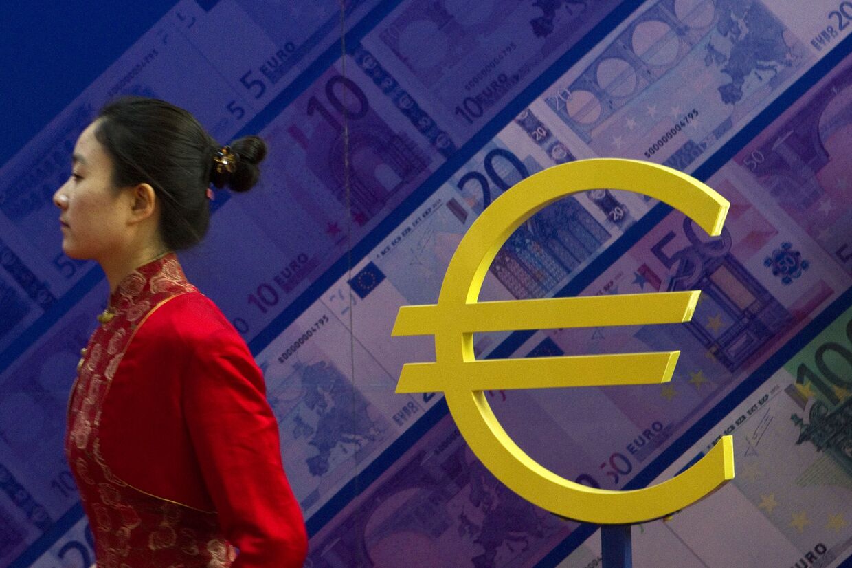 Девушка проходит мимо знака евро на выставке, посвященной валюте в Пекине