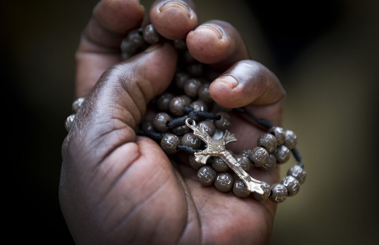 Женщина держит в руке распятие во время мессы в католическом храме в Кампалы в Уганде