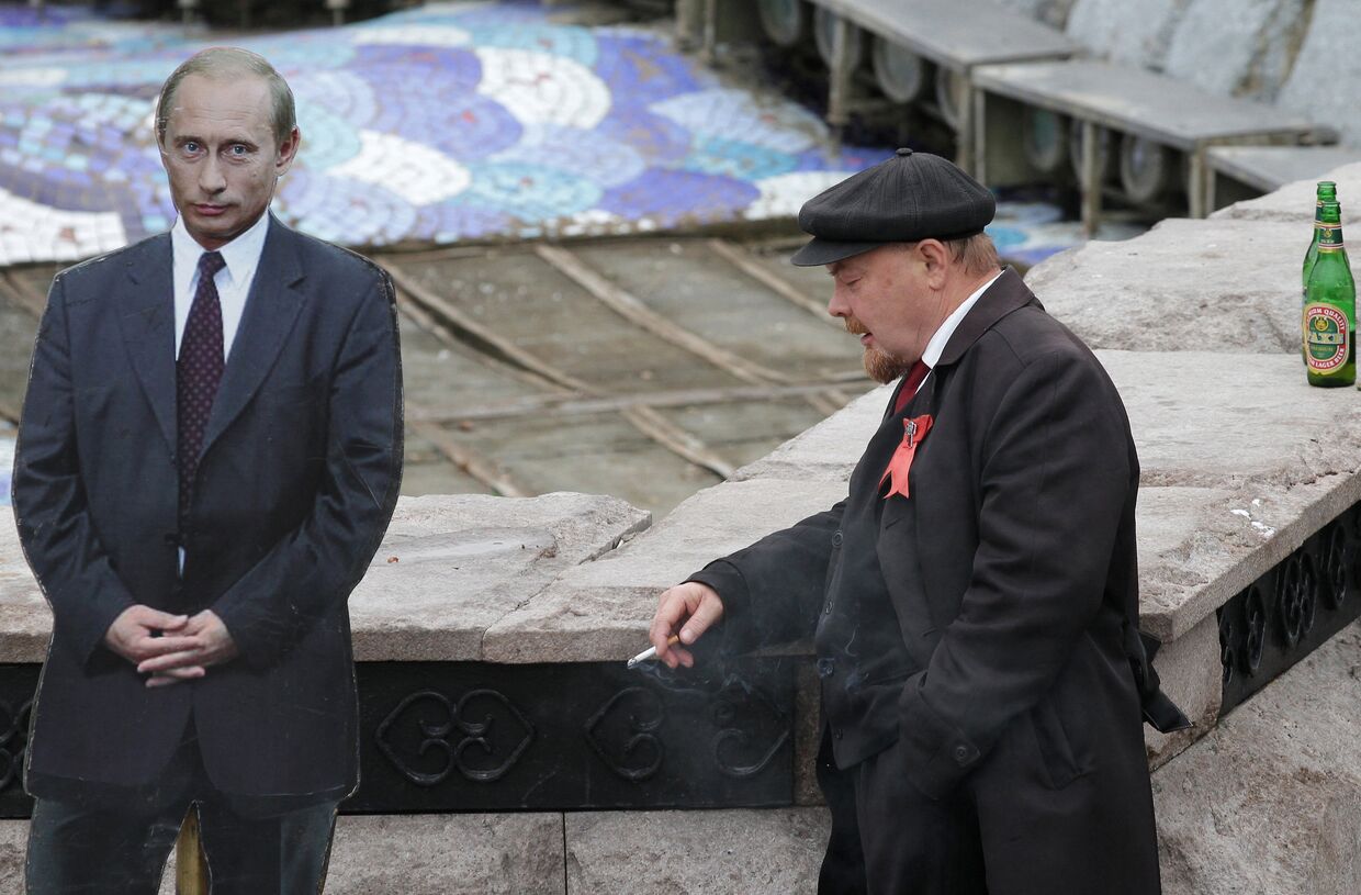 Двойник создателя Советского государства В.И.Ленина курит рядом с фотографией президента РФ Владимира Путина