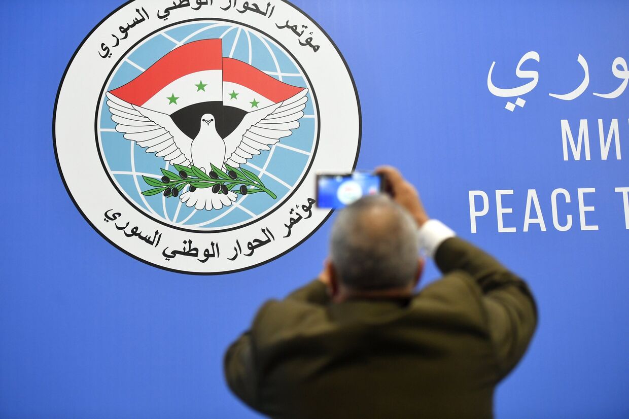 Мужчина фотографирует эмблему конгресса сирийского национального диалога в Сочи
