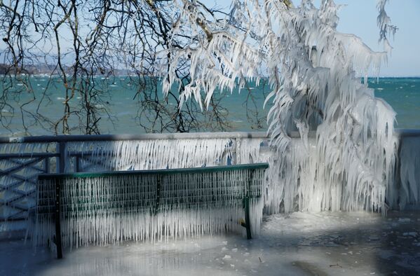 Фотография скамейки, покрытой льдом, снята на берегу замерзшего Женевского озера в Женеве, Швейцария.
