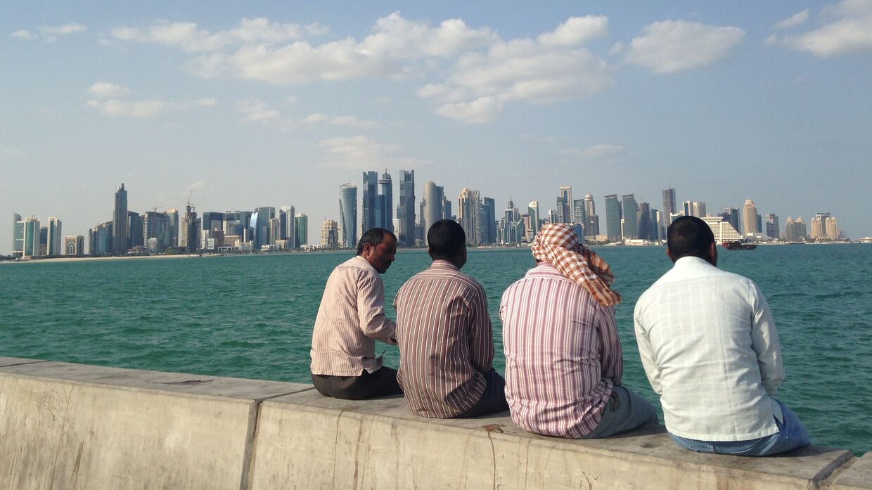 Мужчины сидят на набережной в Дохе, Катар