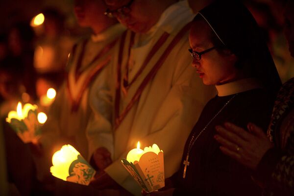 Прихожане держат свечи во время мессы в Страстную субботу накануне Пасхи
