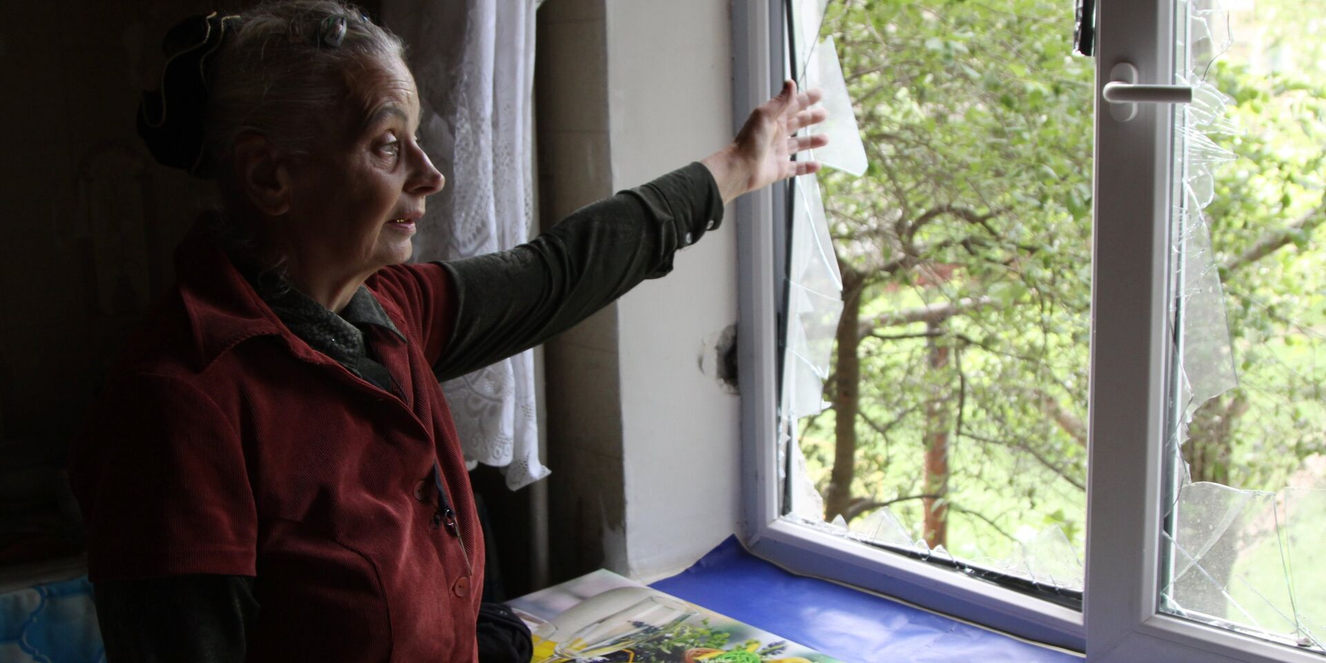 Жительница демонстрирует разбитое окно в жилом доме, пострадавшем в результате обстрела, в поселке Горловка Донецкой области. 21 мая 2018 - ИноСМИ, 1920, 07.05.2023