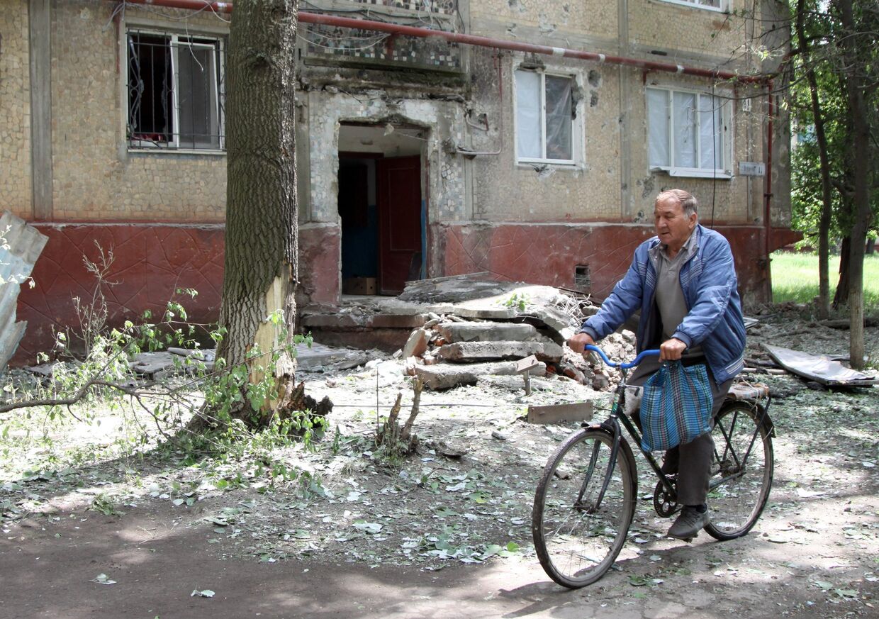 Мужчина едет на велосипеде во дворе жилого дома, пострадавшего в результате обстрела, в поселке Горловка Донецкой области