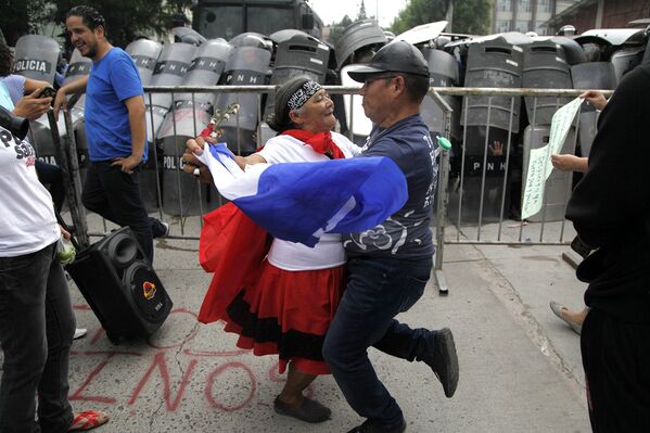 Пара танцует перед полицейской баррикадой во время протеста в Тегусигальпе, Гондурас