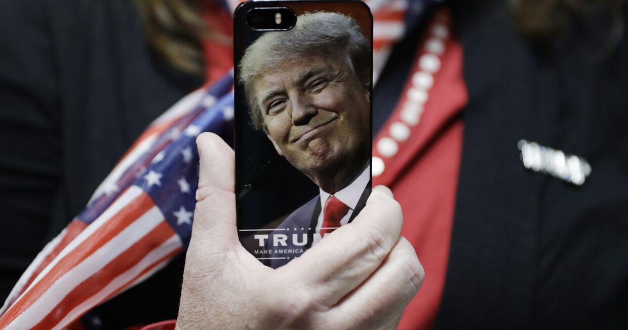 Женщина держит телефон с фотографией Дональда Трампа во время предвыборной кампании в США