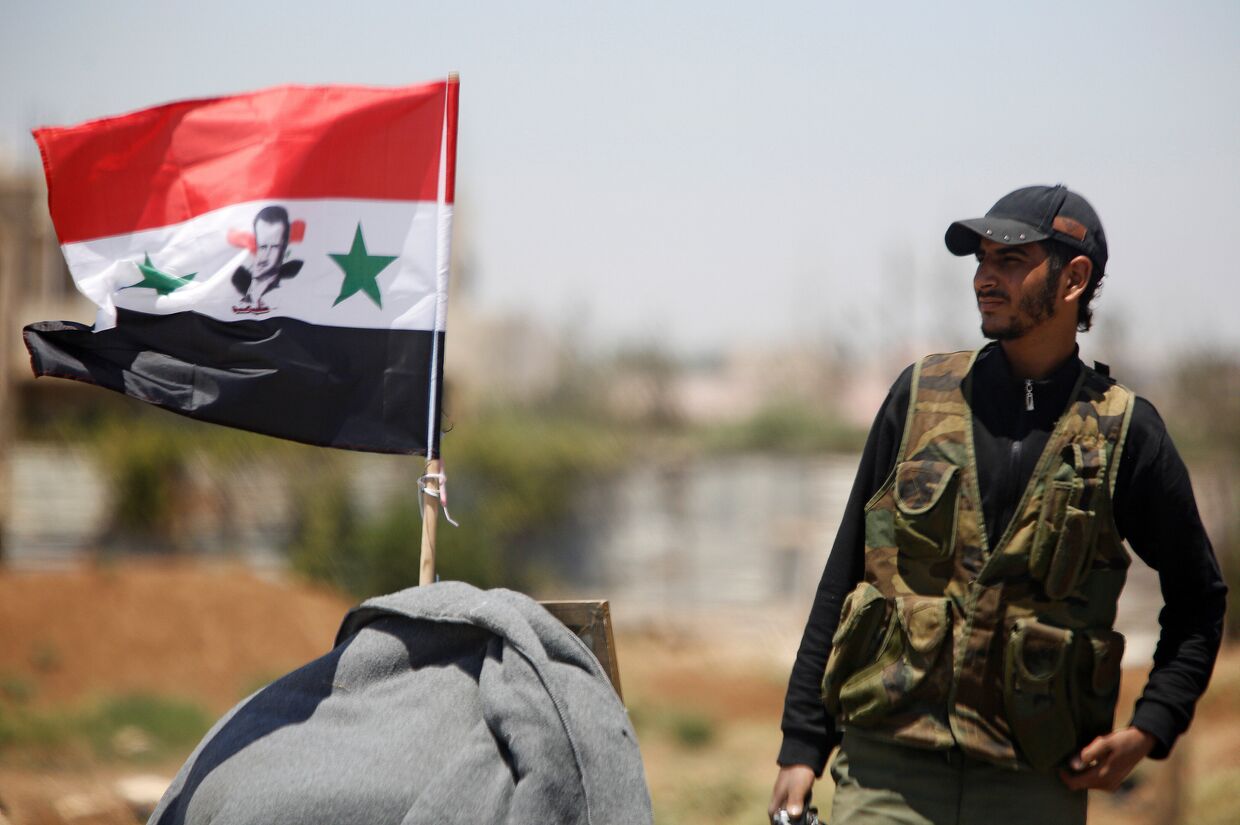 Солдат сирийской армии с флагом Сирии недалеко от Деръа