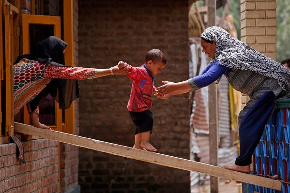 Женщины помогают ребенку перебраться в другой дом во время наводнения в индийском городе Сринагар