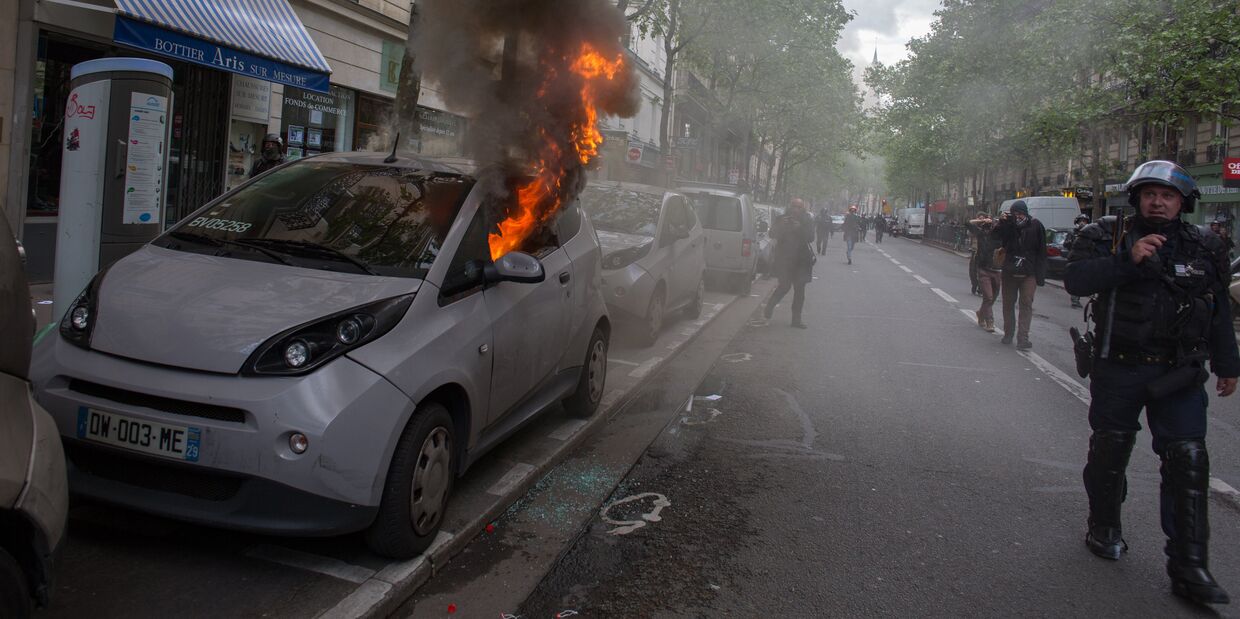 Горящий автомобиль во время беспорядков, возникших во время первомайской демонстрации в Париже