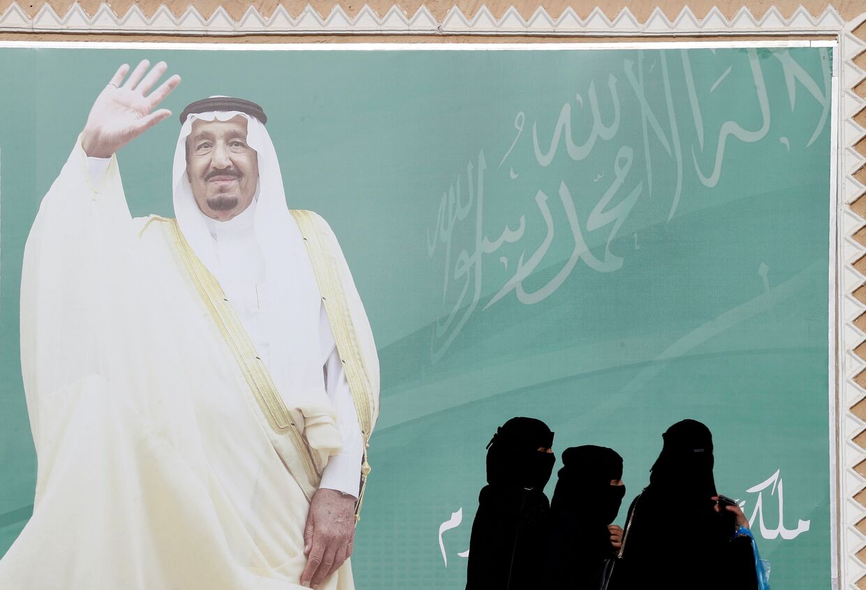 Женщины идут мимо плаката Короля Саудовской Аравии Салмана бин Абдулазиз Аль Сауда в Эр-Рияде