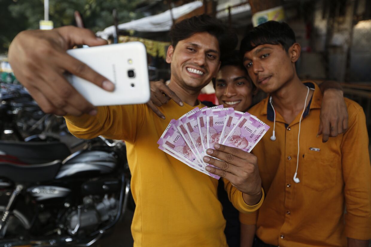Молодые люди фотографируются с купюрами достоинством в 2000 рупий после денежной реформы в Индии