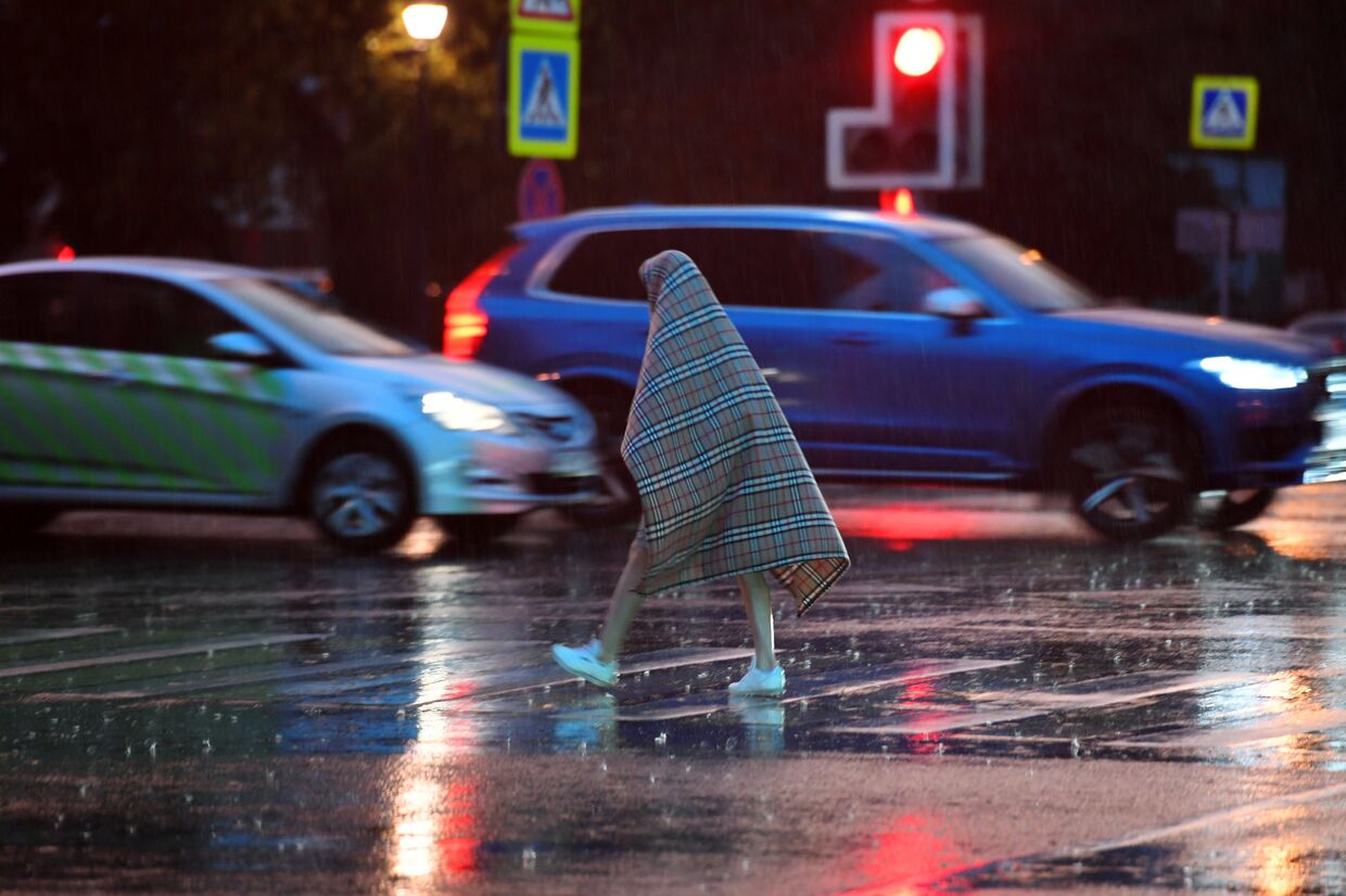 Прохожий переходит дорогу во время дождя, накрывшись пледом