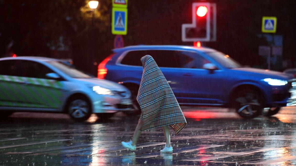 Прохожий переходит дорогу во время дождя, накрывшись пледом