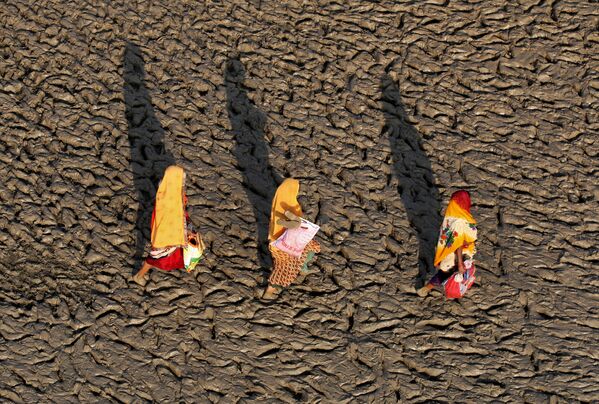Женщины гуляют по илистому берегу реки Ганг в Аллахабаде, Индия