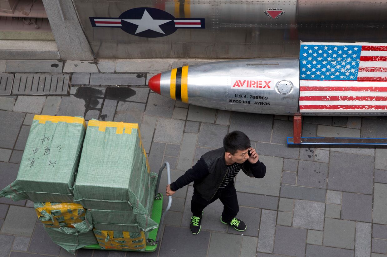 Мужчина с тележкой возле скамейки в виде ракеты с флагом США рядом с магазином в Пекине
