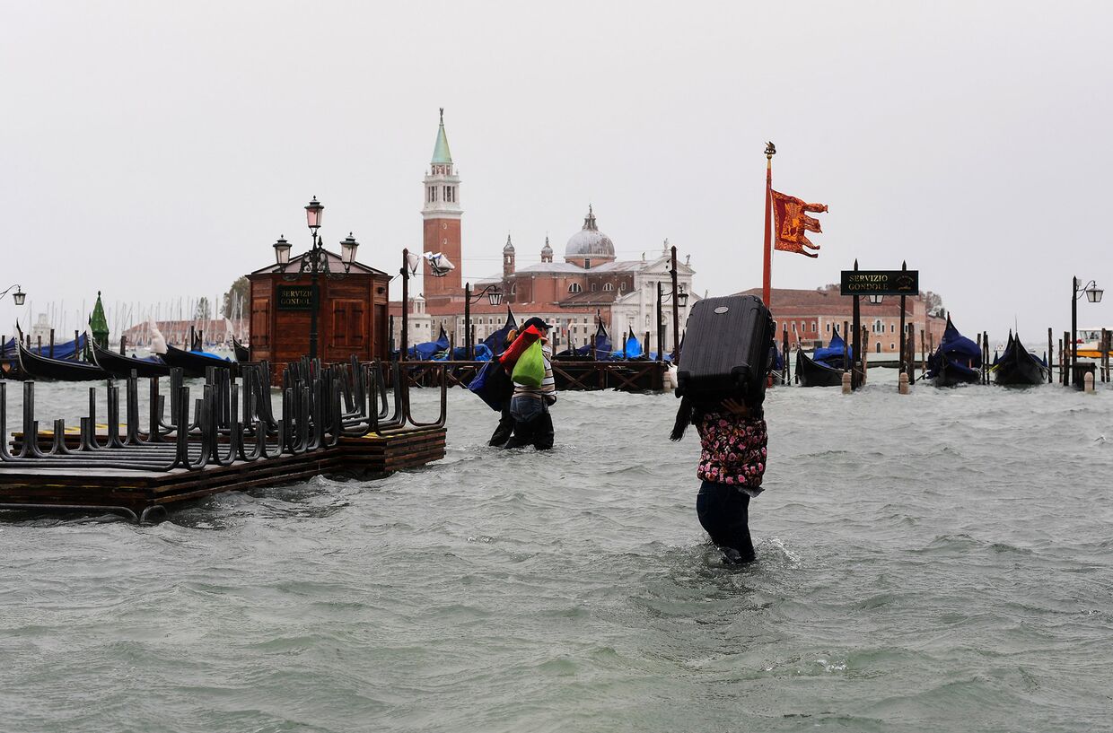 Женщина несет чемодан на затопленной площади Святого Марка в Венеции