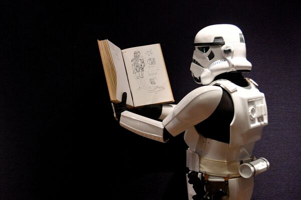 Человек, одетый в костюм штурмовика показывает книгу с иллюстрациями к костюмам «Звездных войн»