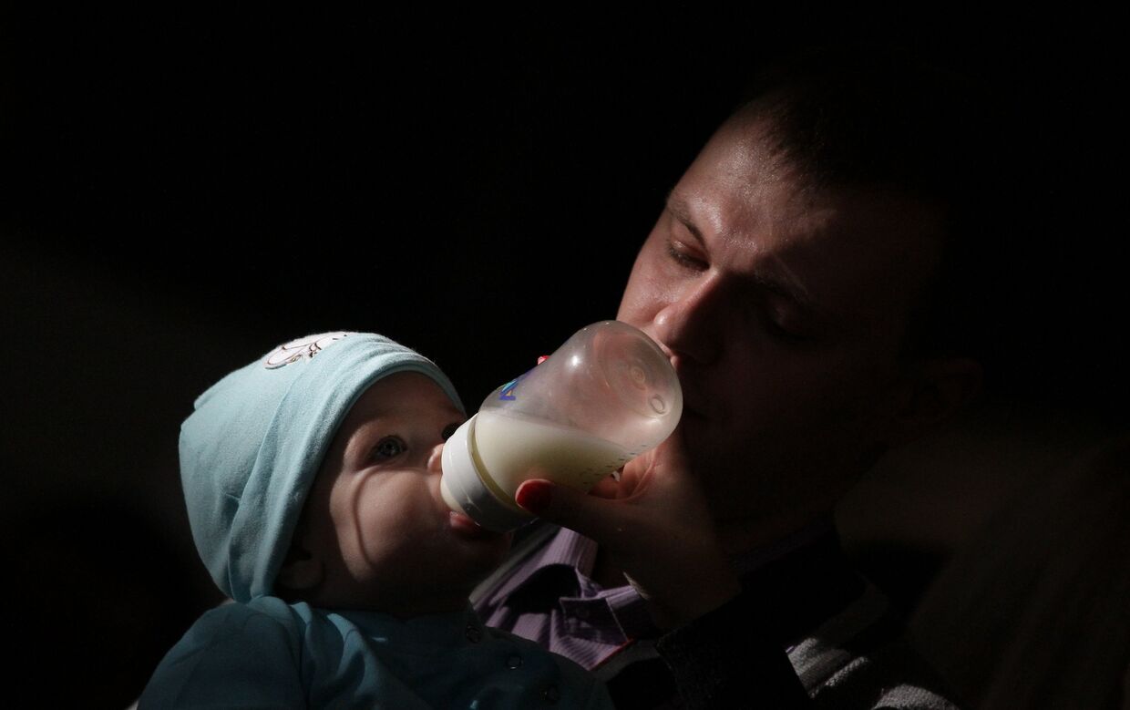 Отец кормит ребенка из из бутылочки на фестивале BabyFest в Сокольниках
