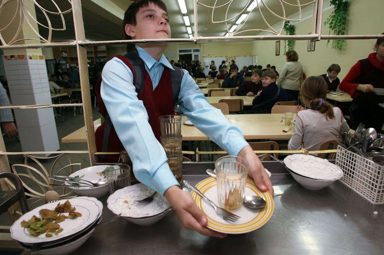 Школьник убирает за собой посуду в столовой