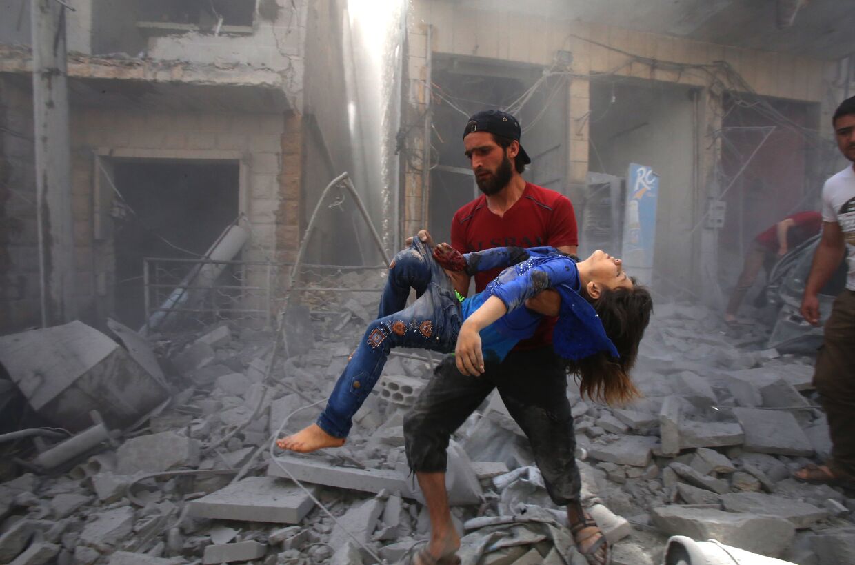 Мужчина спасает девочку из развалин после авианалета в Идлибе, Сирия