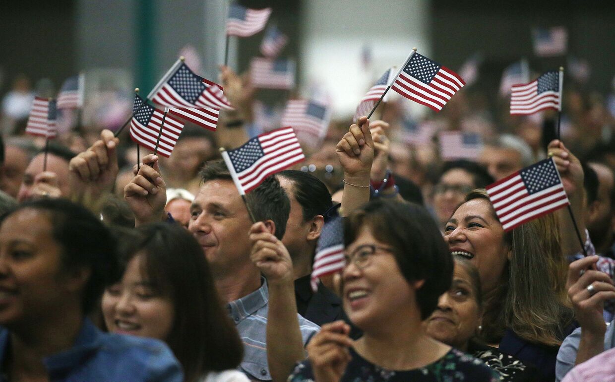 Люди машут американскими флагами на церемонии натурализации в Лос-Анджелесе