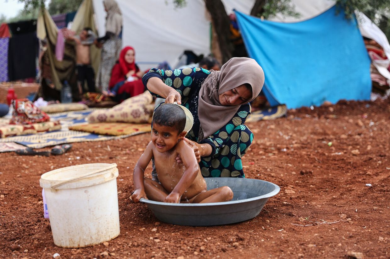 Женщина моет ребенка в тазу в лагере для беженцев неподалеку от Идлиба, Сирия