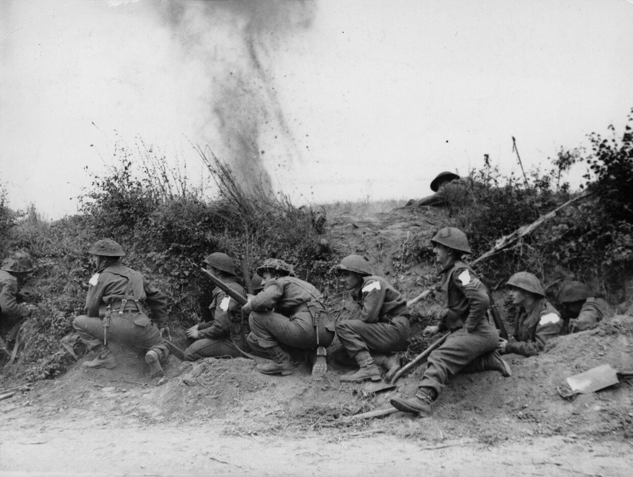 Британские и канадские войска прячутся за песчаной дюной во время вторжения союзников в Нормандию в июне 1944 года
