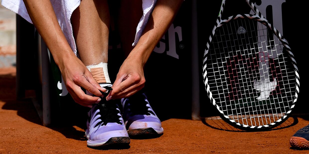 Теннисистка завязывает шнурки на кроссовках перед матчем