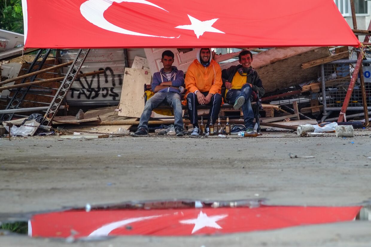 Молодые люди сидят под флагом Турции на площади Таксим в Стамбуле