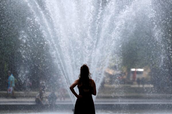 Женщина охлаждается возле фонтана в жаркий летний день в Брюсселе, Бельгия
