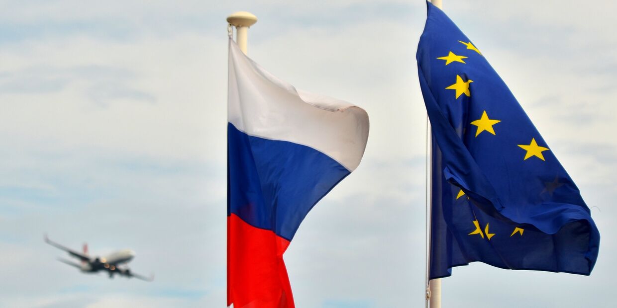 Флаги России, ЕС и Франции на набережной Ниццы. На дальнем плане - самолет заходит на посадку в международный аэропорт Ниццы.