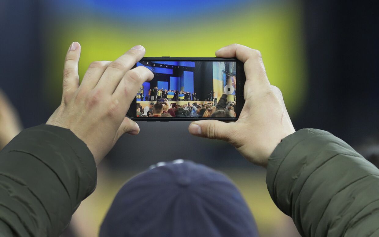 Мужчина фотографирует дебаты между Петром Порошенко у Владимиром Зеленским в Киеве