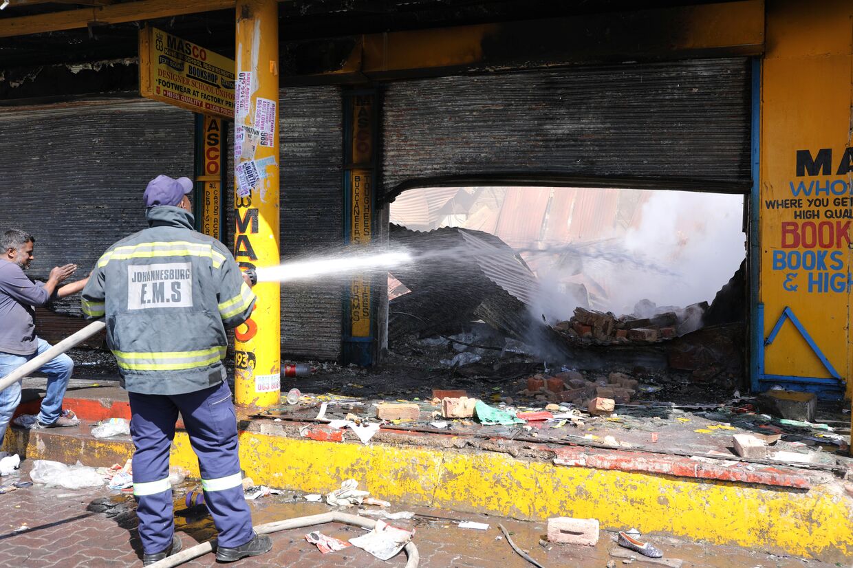 Пожарный заливает сгоревший магазин после ночных волнений, Йоханнесбург