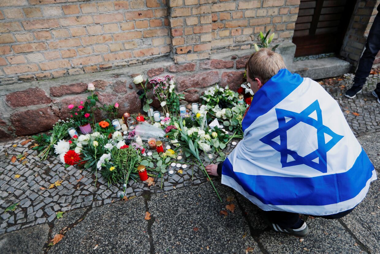 Человек с флагом Израиля возлагает цветы к месту стрельбы у синагоги в городе Галле, Германия