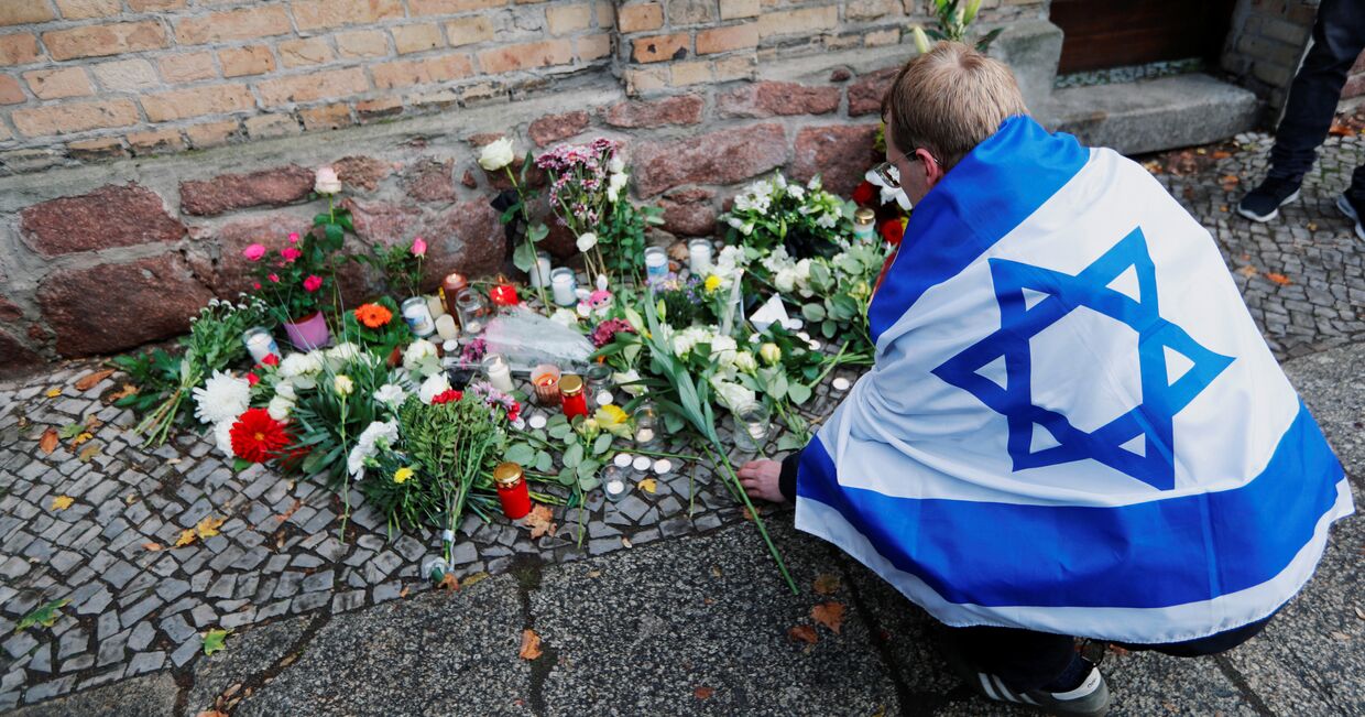 Человек с флагом Израиля возлагает цветы к месту стрельбы у синагоги в городе Галле, Германия