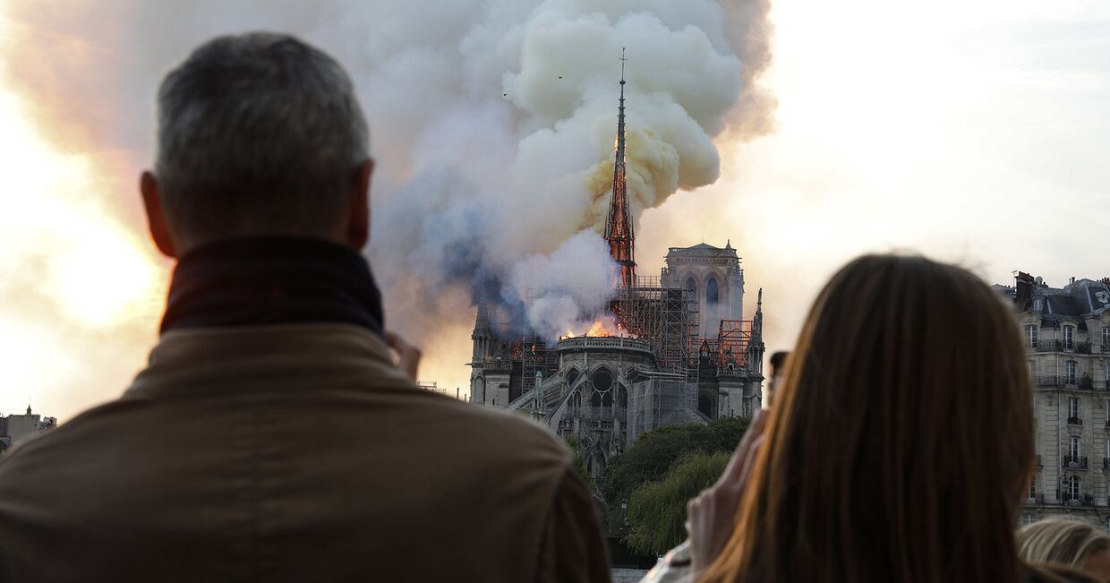 Люди наблюдают как пламя охватывает крышу Собора Парижской Богоматери в Париже