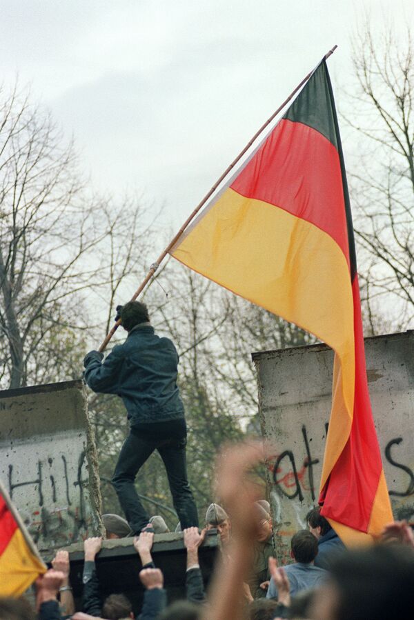 Житель Западного Берлина передает флаг через Берлинскую стену 11 ноября 1989 года