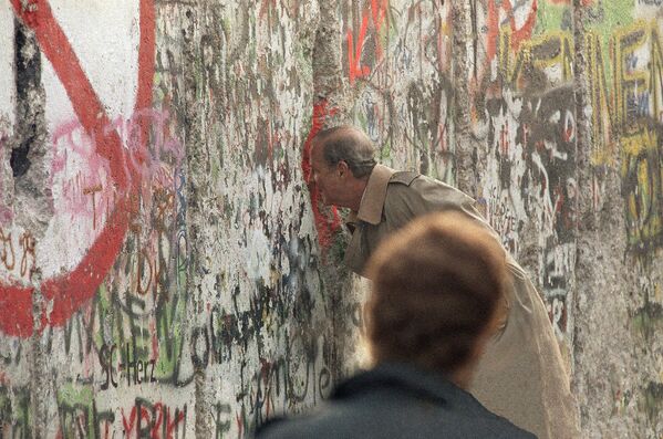 Госсекретарь США Джеймс Бейкер III смотрит через разлом в Берлинской стене на Потсдамской площади