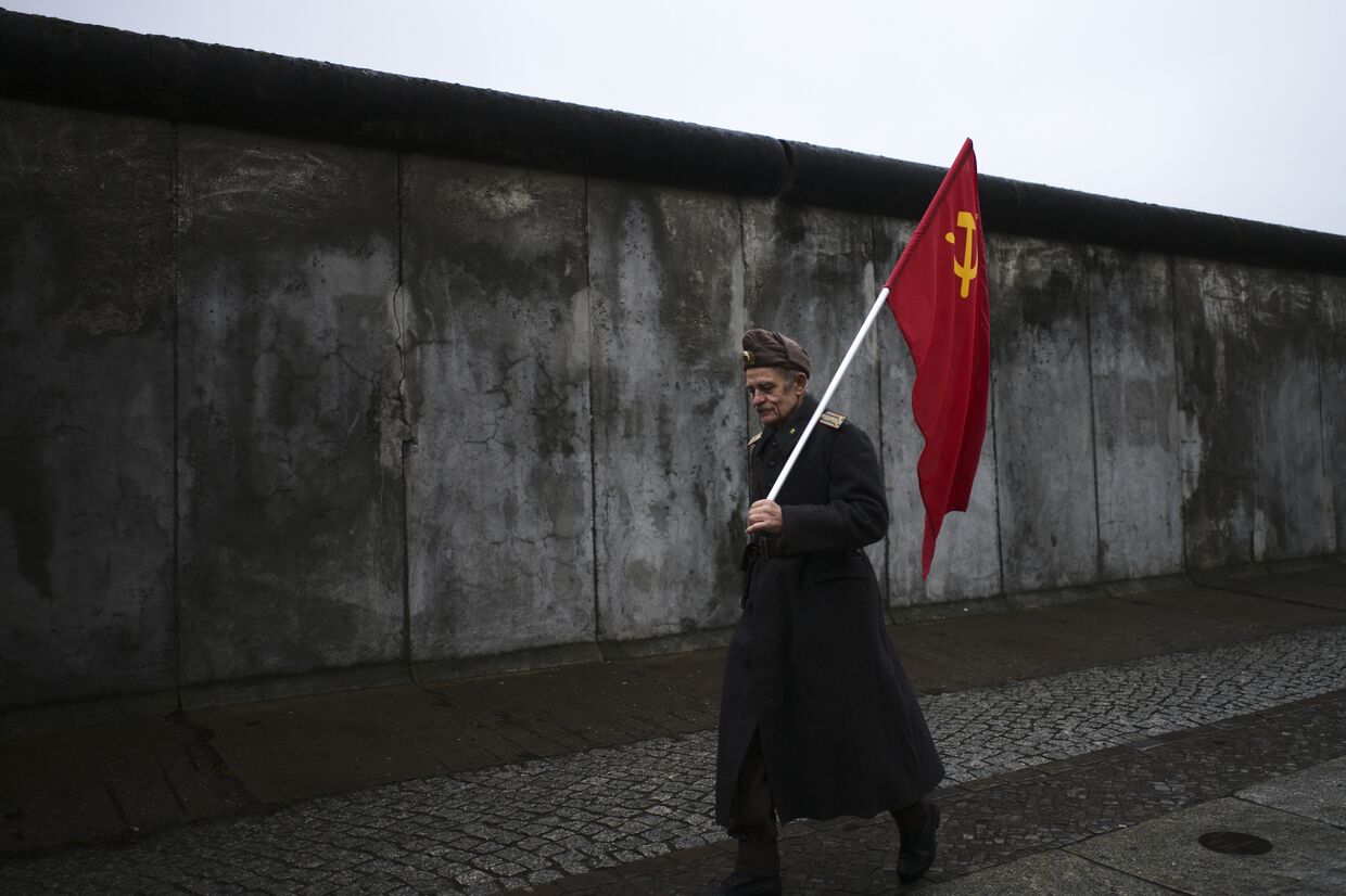 Пожилой человек с советским флагом на фоне Берлинской стены