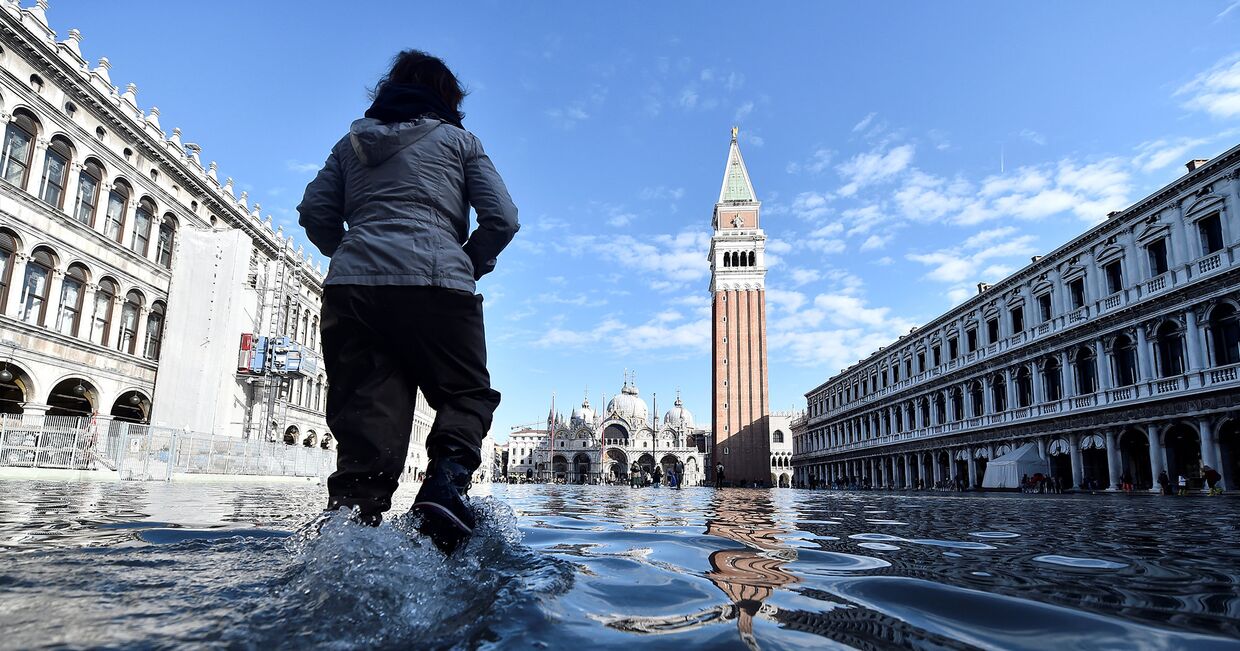 Женщина идет по затопленной площади Святого Марка в Венеции, Италия