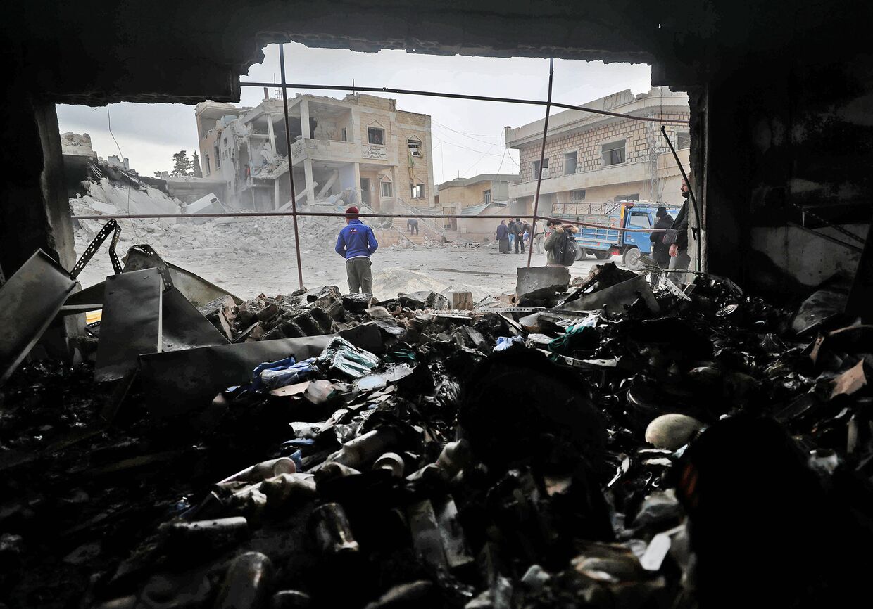 Сирийцы среди обломков после воздушных ударов в городе Кансафра на юге провинции Идлиб
