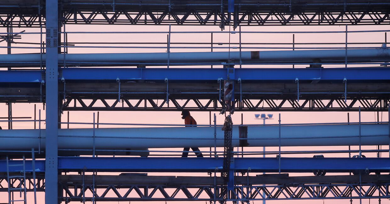 Строитель идет по мосту с трубопроводами на стройплощадке Амурского газоперерабатывающего завода, входящего в проект «Сила Сибири» Газпрома