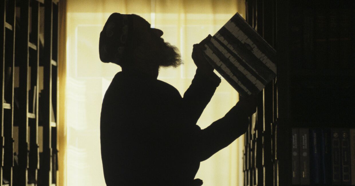 Пожилой таджик у книжных полок в своем доме